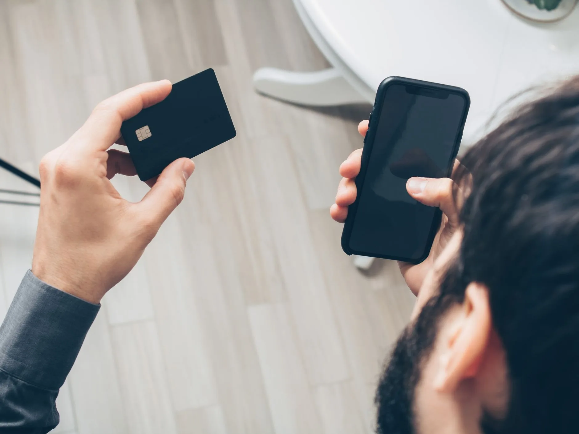 Homem segurando um cartão de crédito e um celular, fazendo um pagamento online