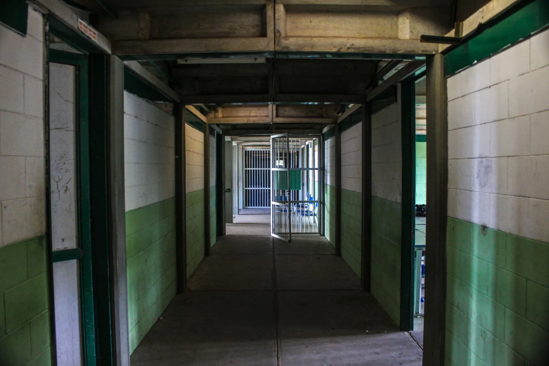 Corredor vazio de uma unidade prisional, com portas de celas abertas dos dois lados