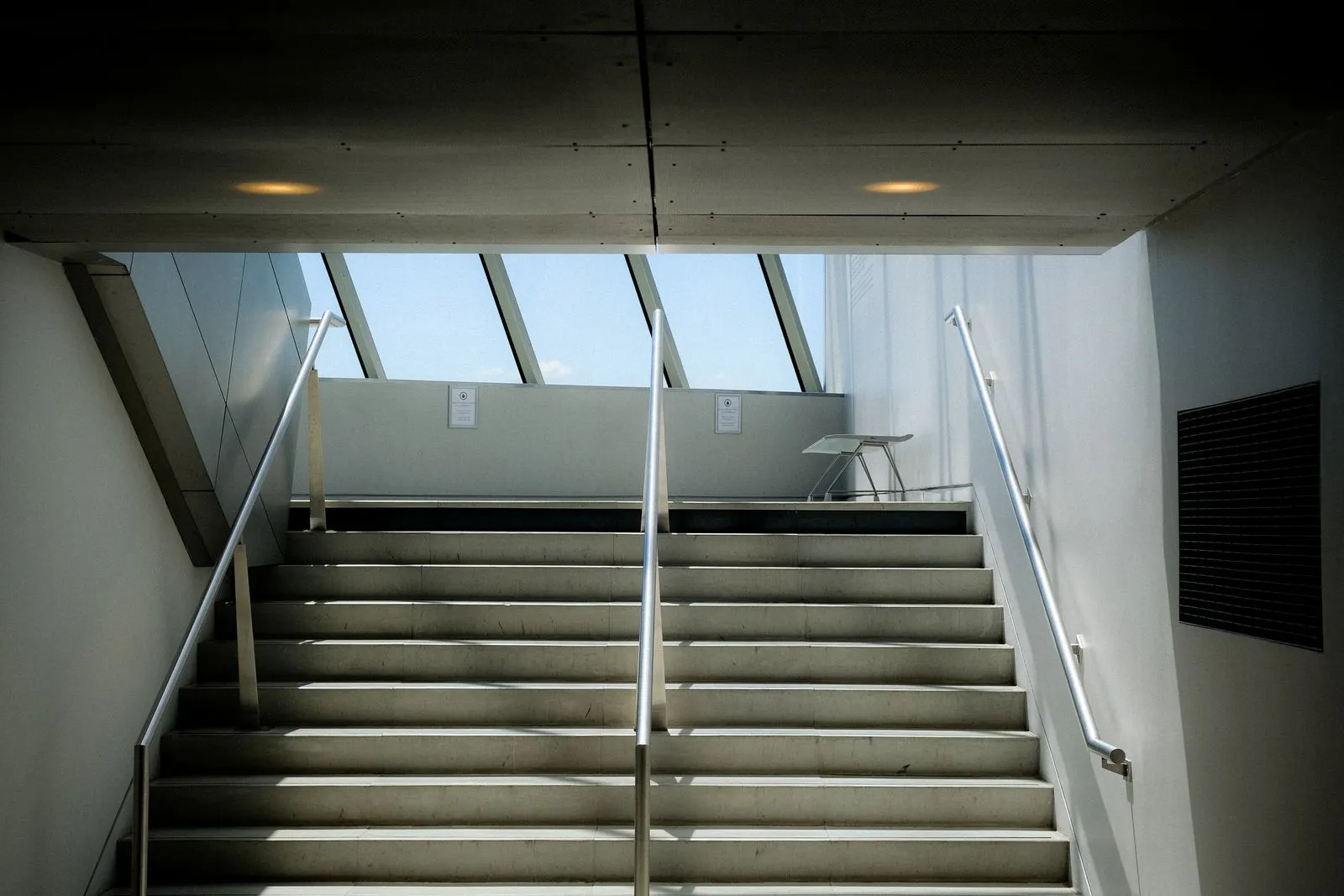 Escada de concreto com corrimão subindo em direção a uma claraboia iluminada